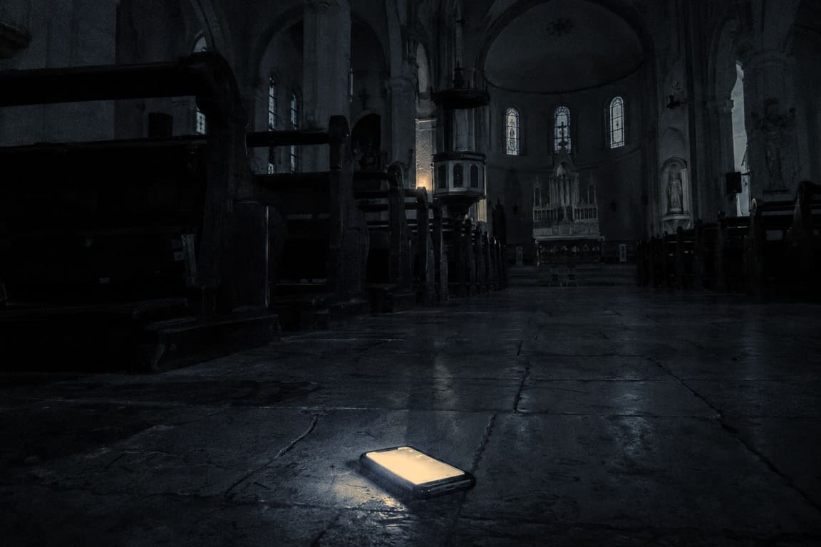An empty church at night. On the stone floor of the aisle, a phone lies face up, its screen still on.